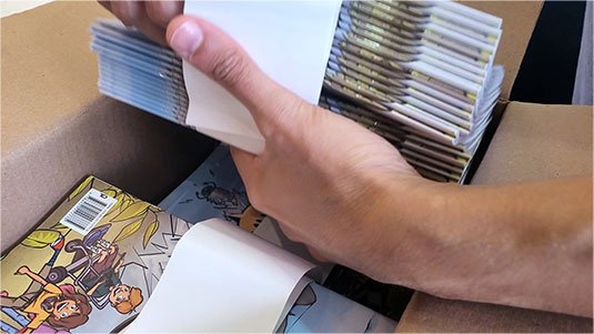 mão tirando revistinhas Salve Rio! de uma caixa